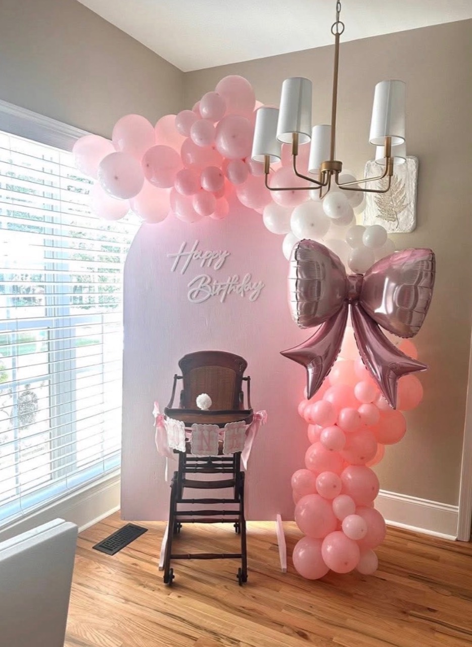 Pink first birthday balloon backdrop with a large bow